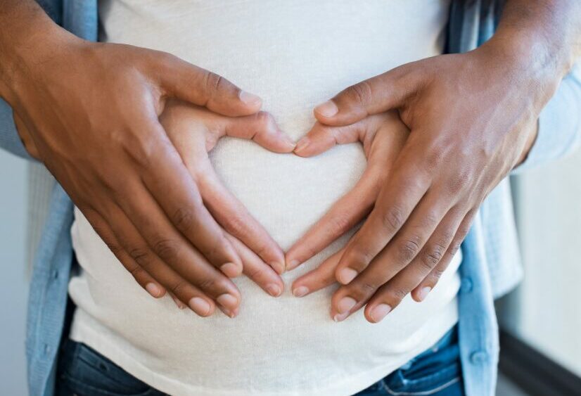 couples hands making heart over pregnant belly